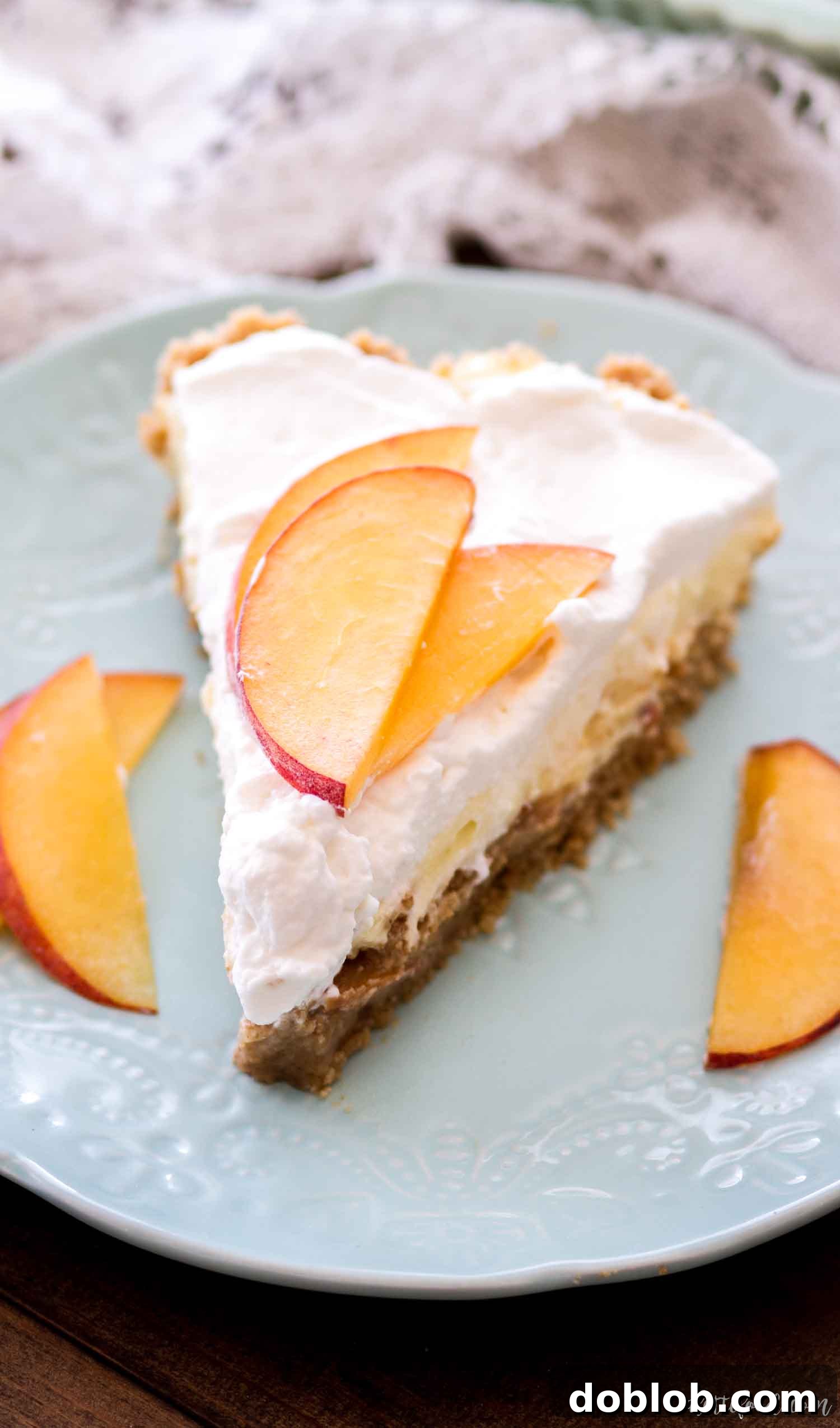 A perfect slice of No Bake Peaches and Cream Pie on a white plate, showcasing its layered filling and graham cracker crust.