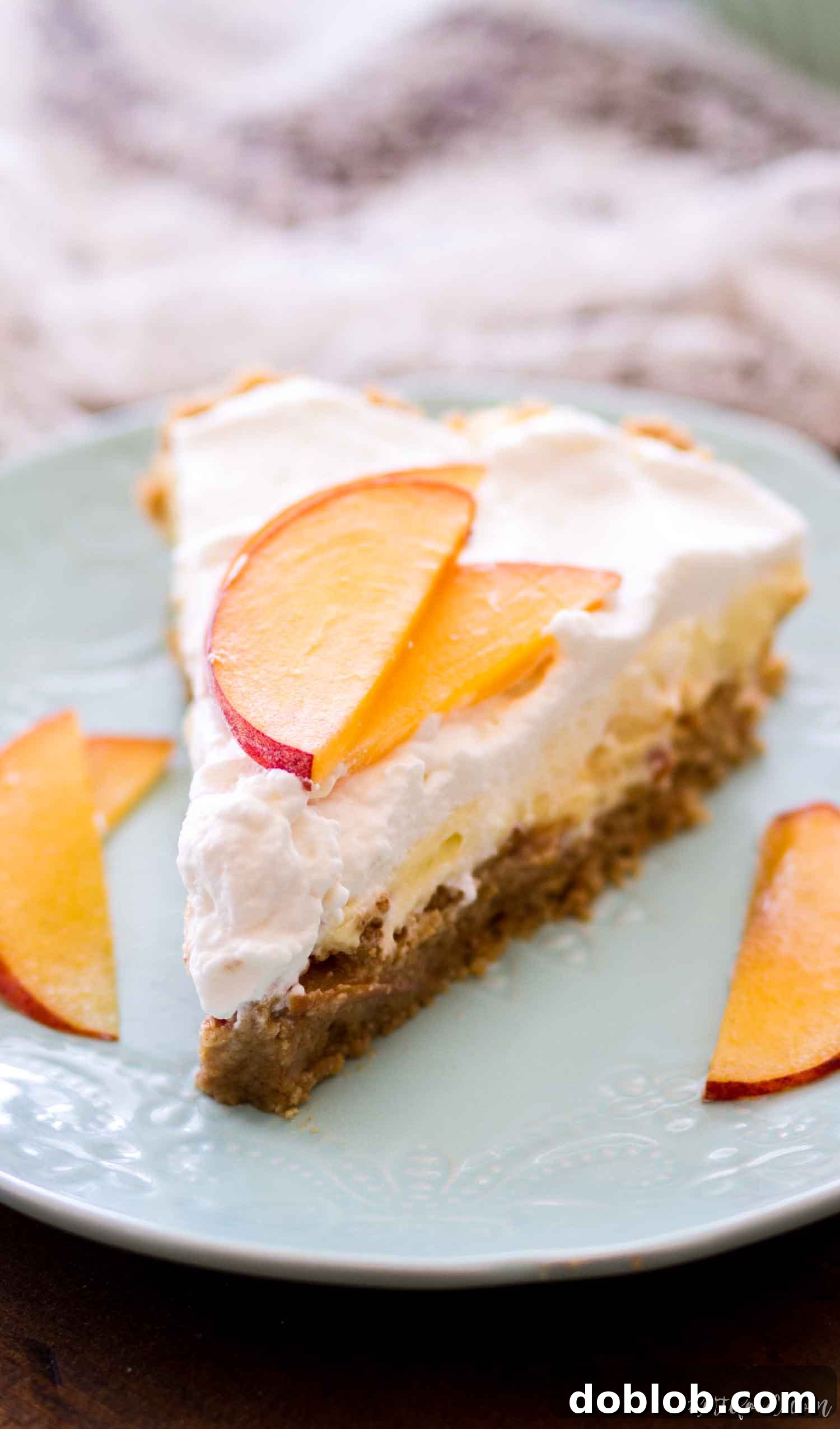 A delectable slice of No Bake Peach Pie on a teal plate, revealing layers of peach filling, vanilla cream, and a crunchy graham cracker base.