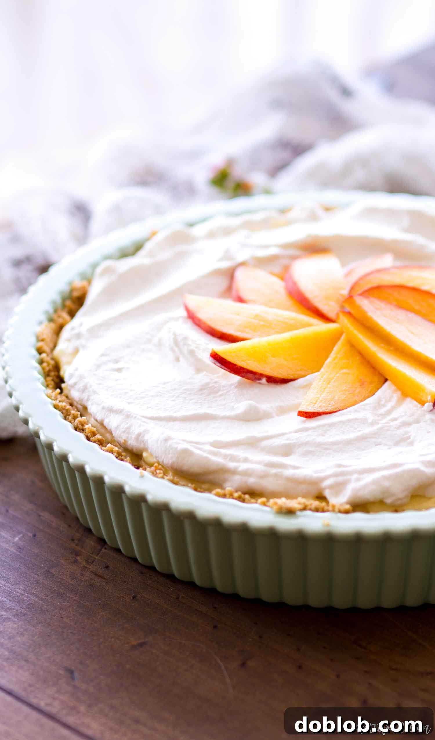 Whole No Bake Peach Pie in a green ceramic pie dish, showcasing its perfect layers and inviting fresh peaches.