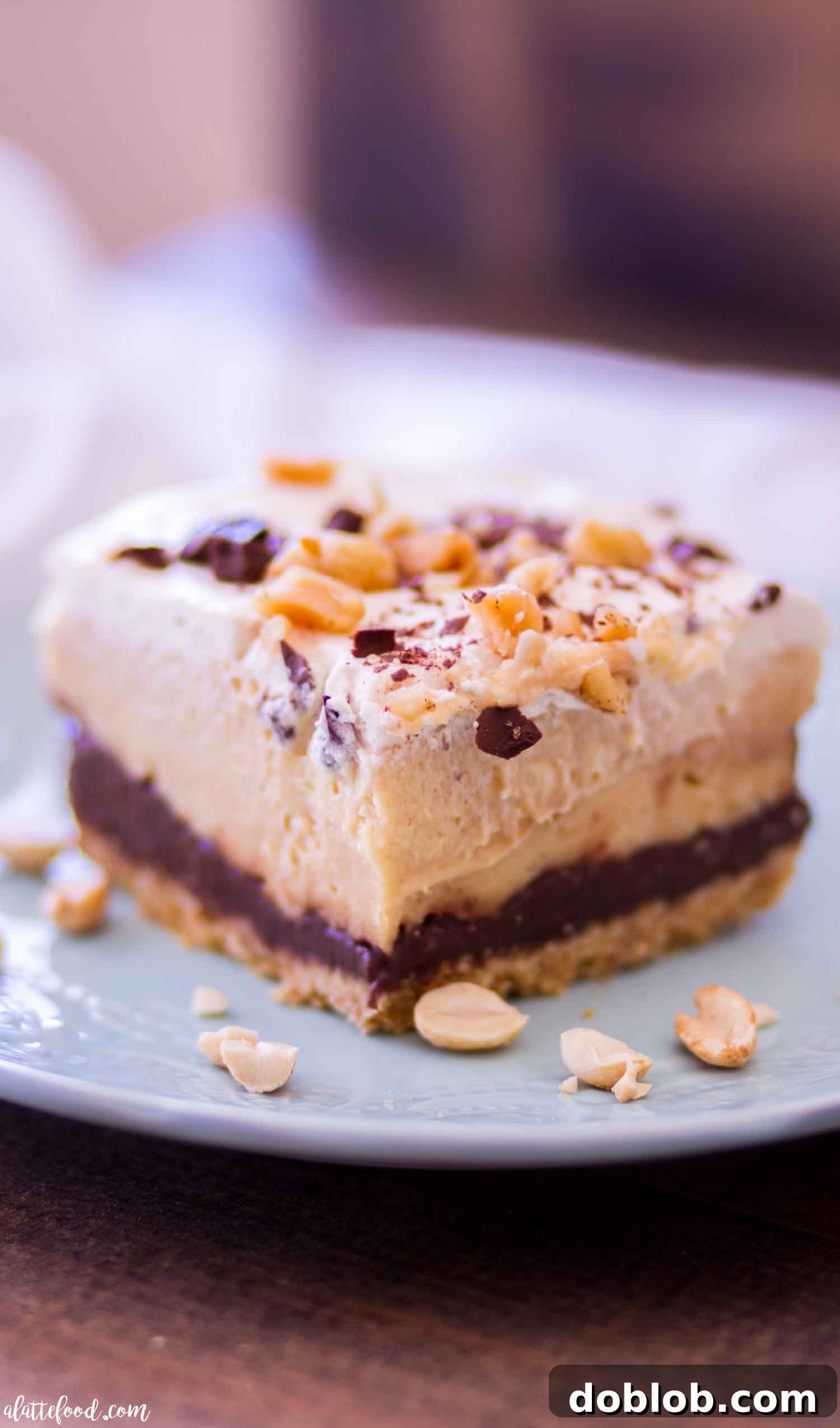 Delicious no-bake chocolate peanut butter pie bar on a blue plate, showing layers of crust, ganache, peanut butter cream, and whipped cream.