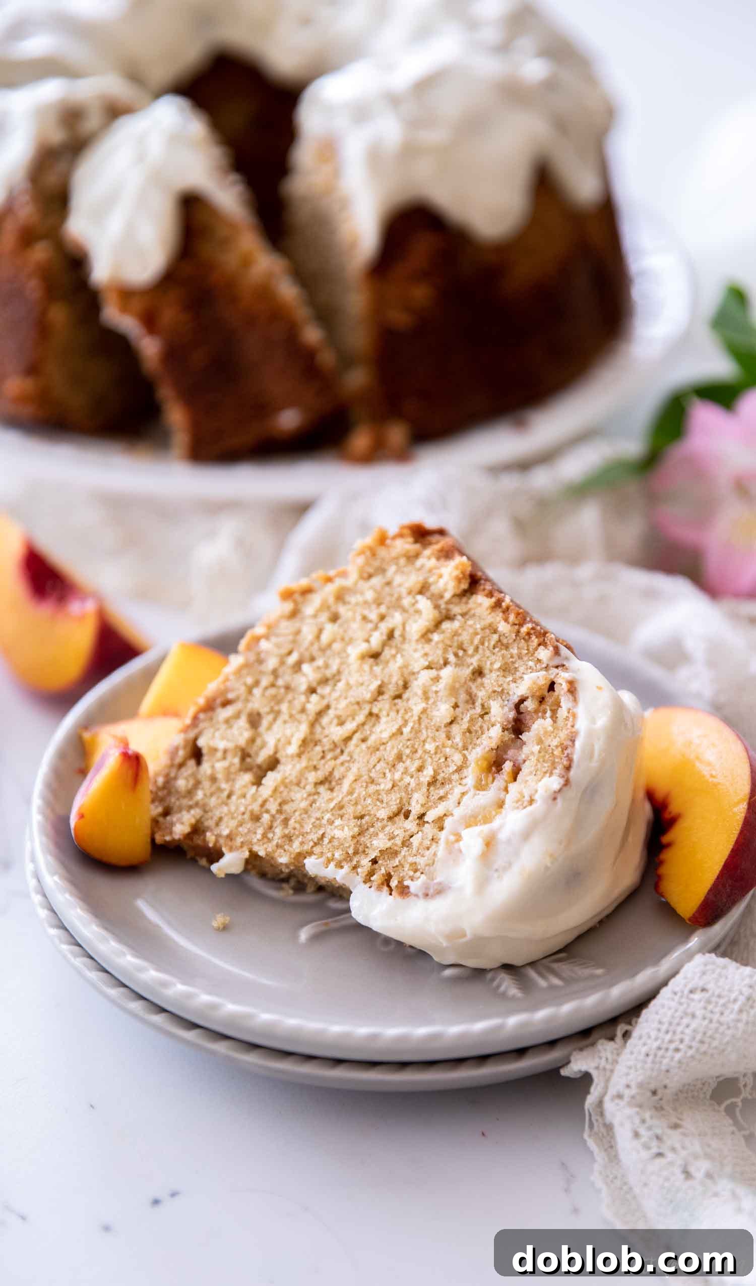 A slice of moist peach pound cake on a gray plate, topped with a luscious cream cheese glaze.
